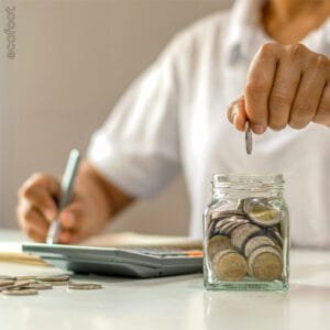 A person putting coins in a white transparent jar while calculating expenses.