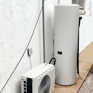 Outdoor heat pump water heater system installed against a wall in a residential property.