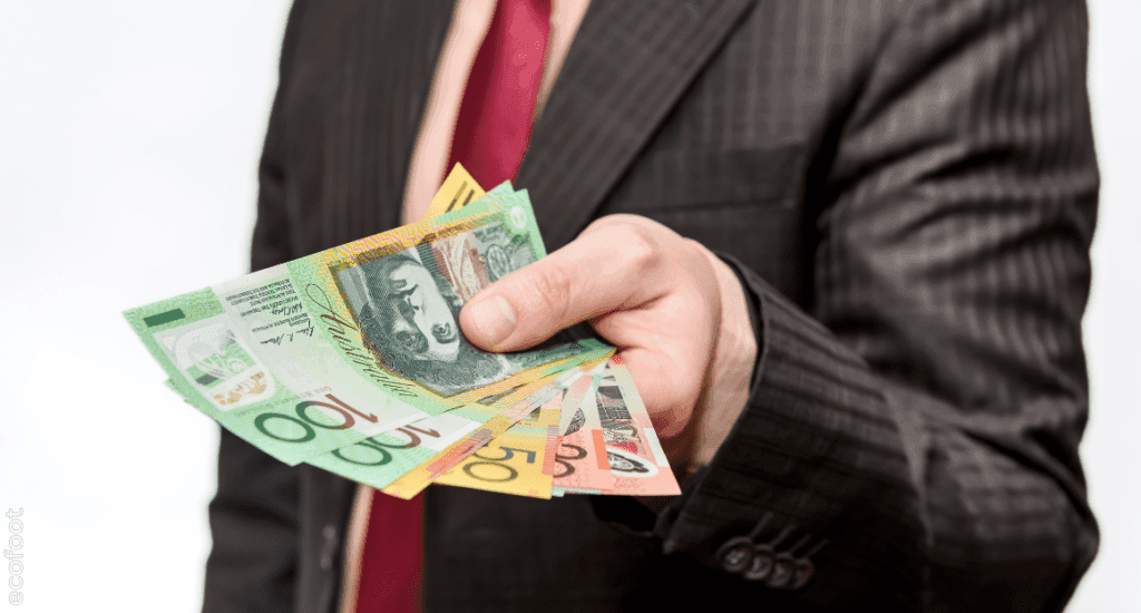 Businessman in a suit holding Australian dollar banknotes, symbolising government rebates and financial savings from energy upgrades.