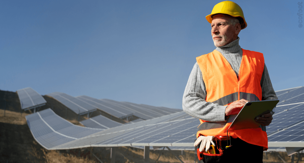Solar technician wearing a safety vest and helmet inspecting large commercial solar panel arrays outdoors.