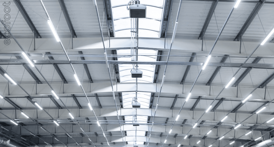 Commercial warehouse ceiling with bright, energy-efficient LED lighting installed under high metal truss roofing.